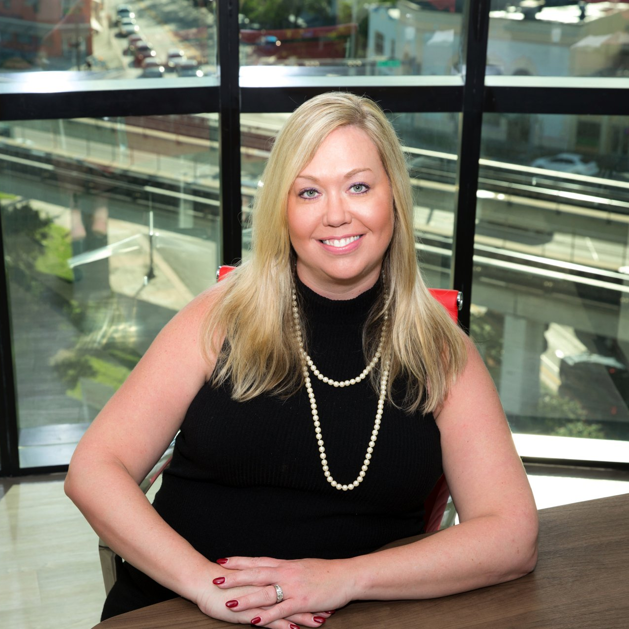 A woman is sitting at a table in front of a window and smiling