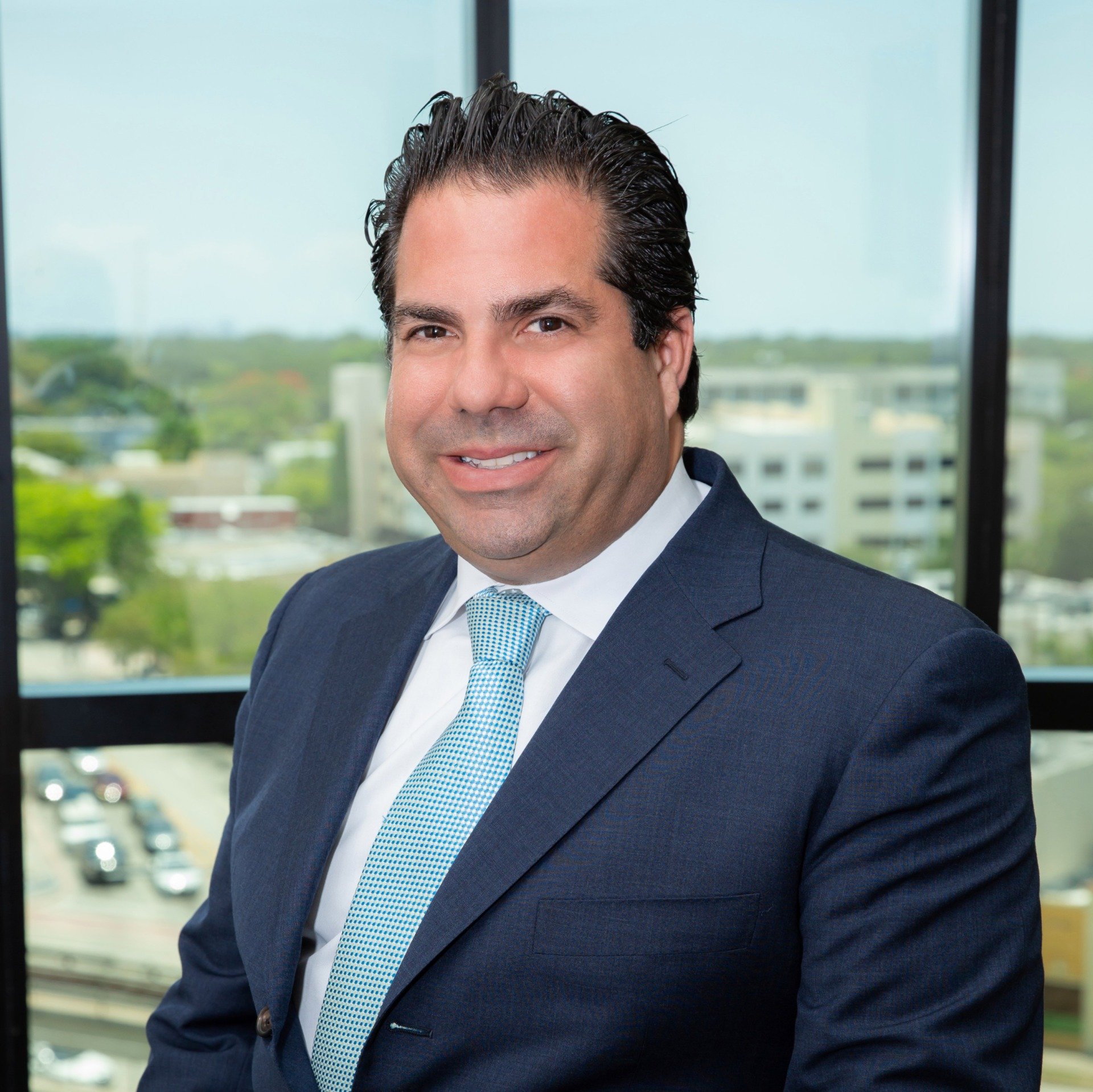 A man in a suit and tie is sitting in front of a window.