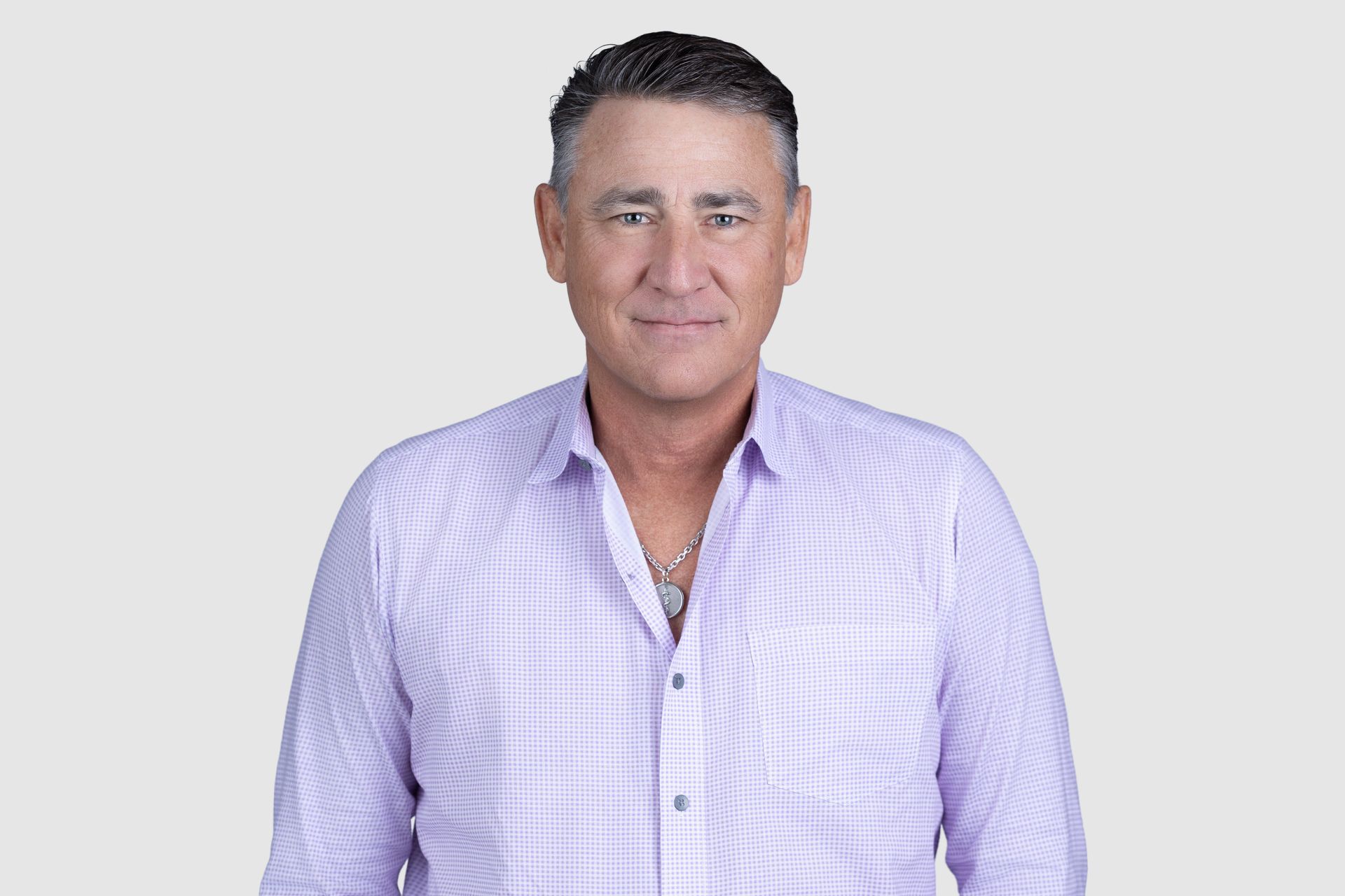 A man in a suit and pink tie is sitting in front of a window.