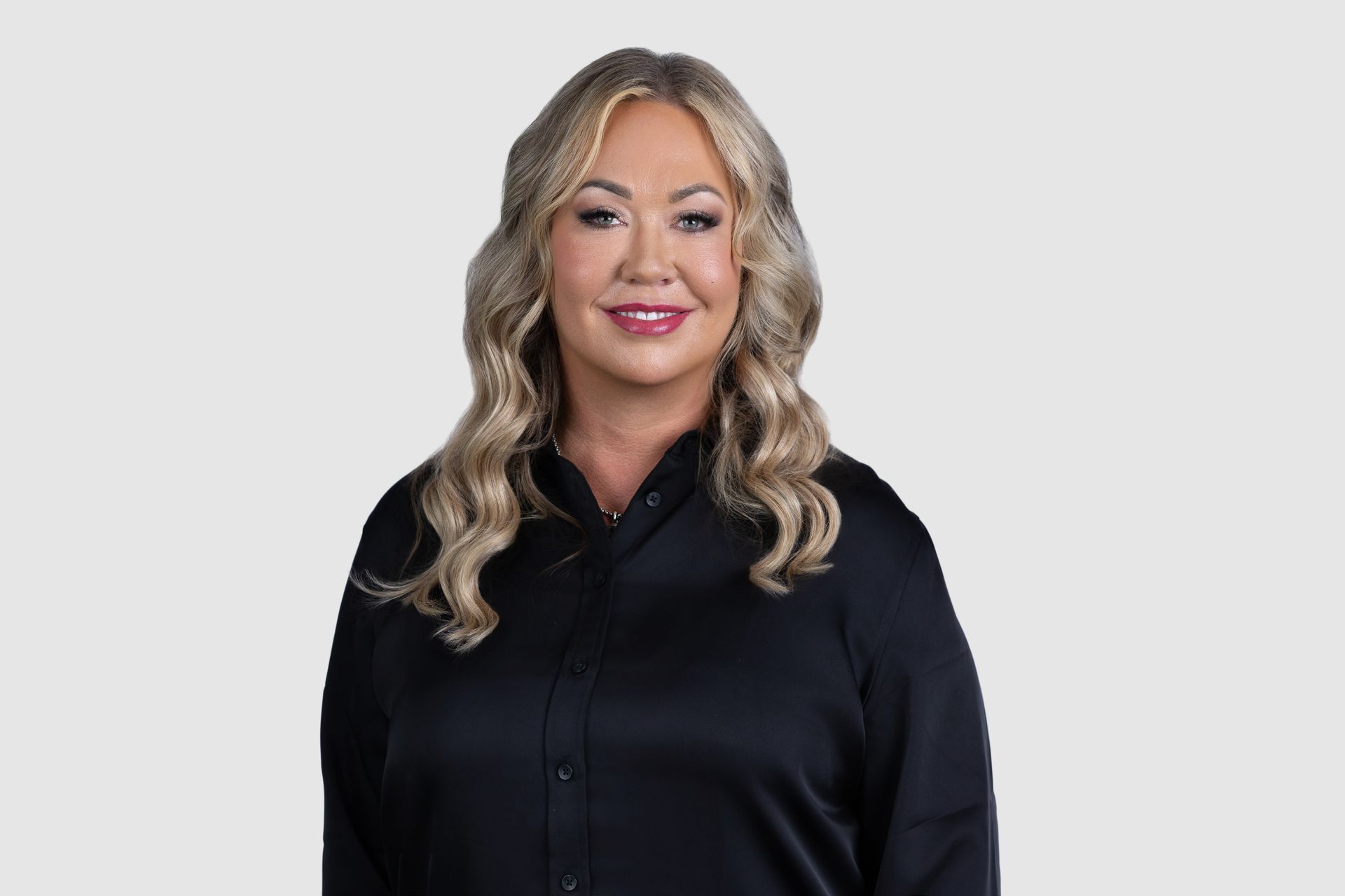 A woman is sitting at a table in front of a window and smiling