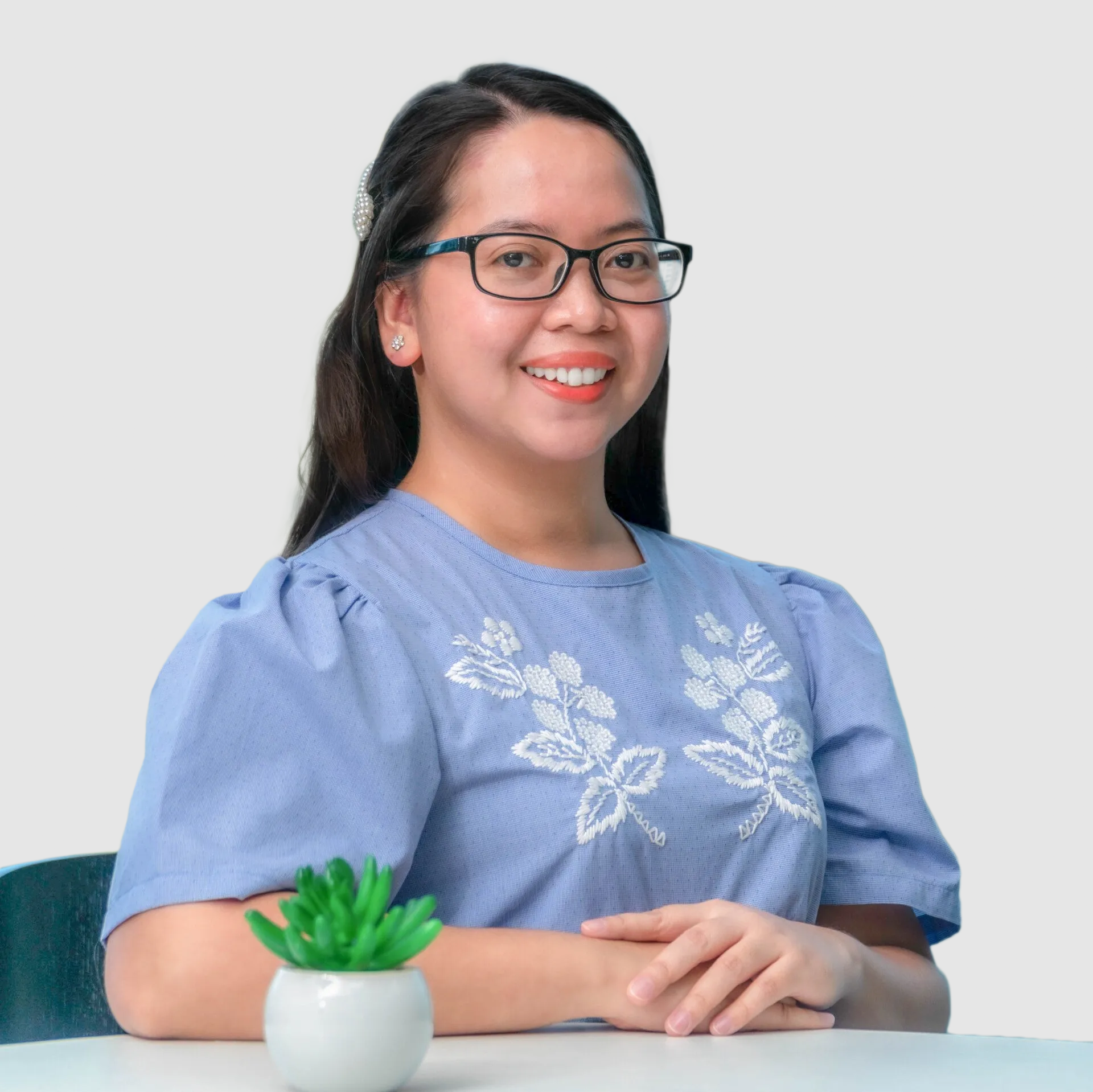 A woman wearing glasses is sitting at a table with a potted plant.