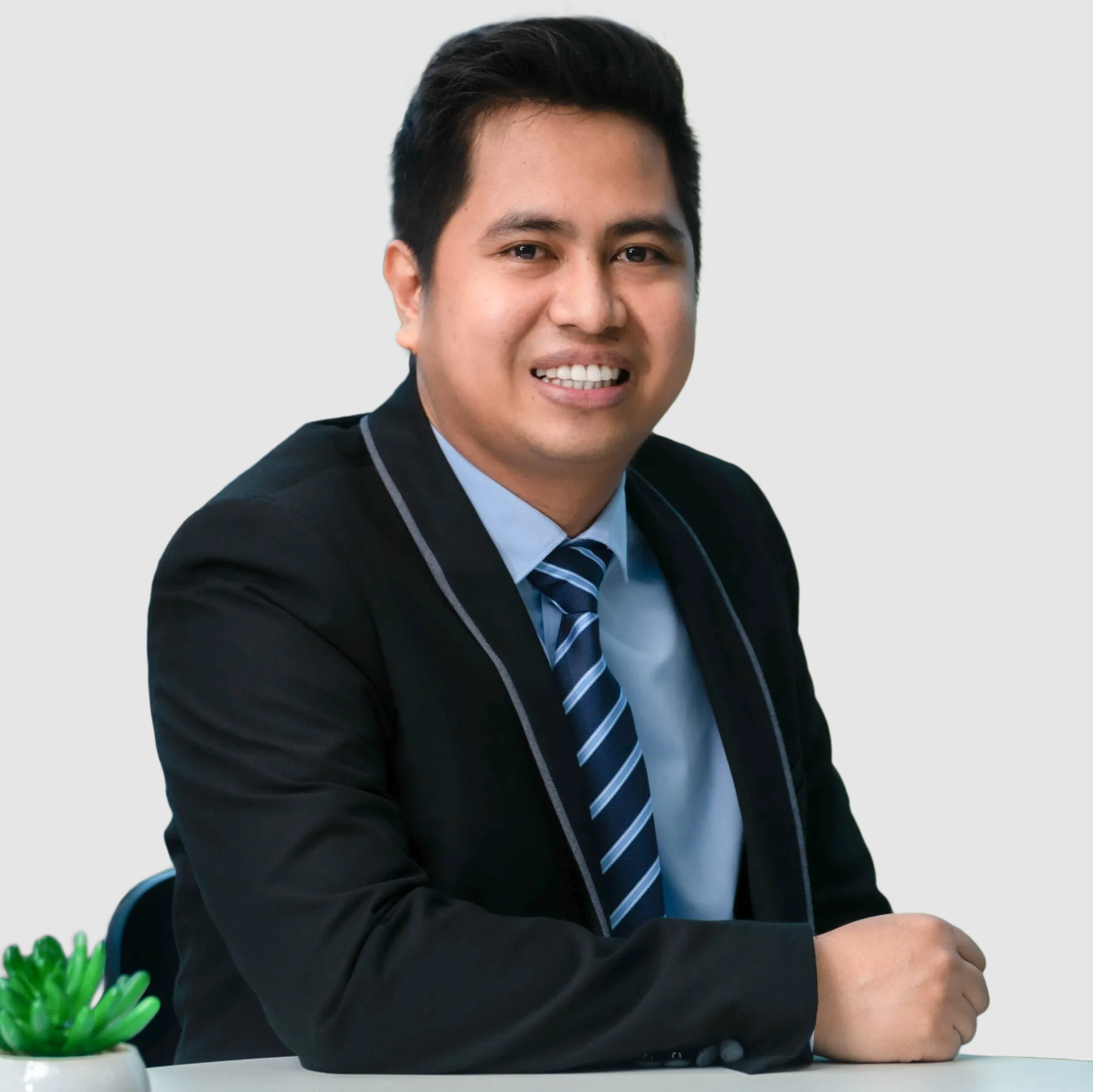 A man in a suit and pink tie is sitting in front of a window.
