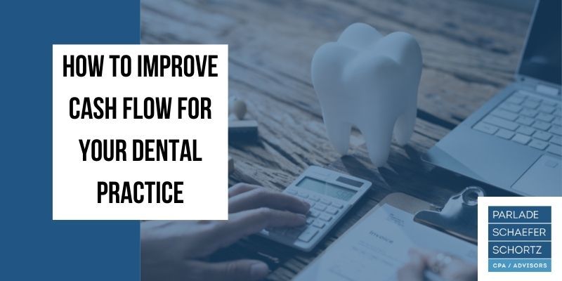 A person is using a calculator next to a tooth on a wooden table.