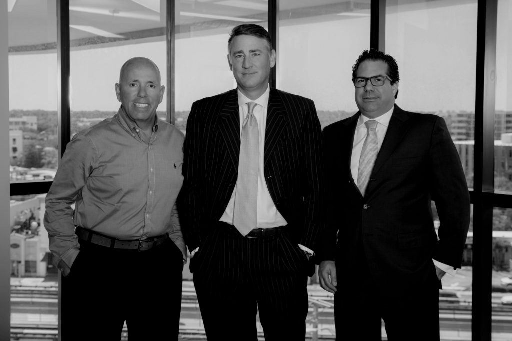 Three men in suits and ties are standing next to each other in front of a window.
