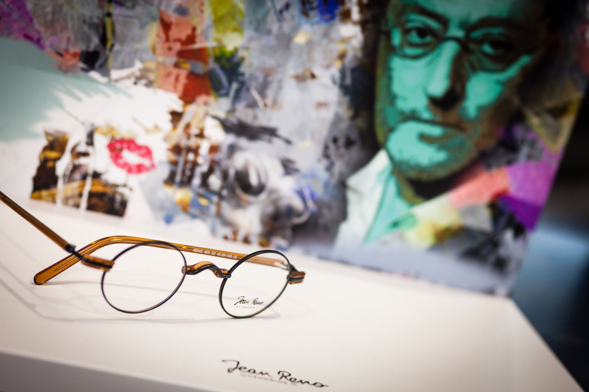 Une paire de lunettes est posée sur une table devant un tableau de John Lennon