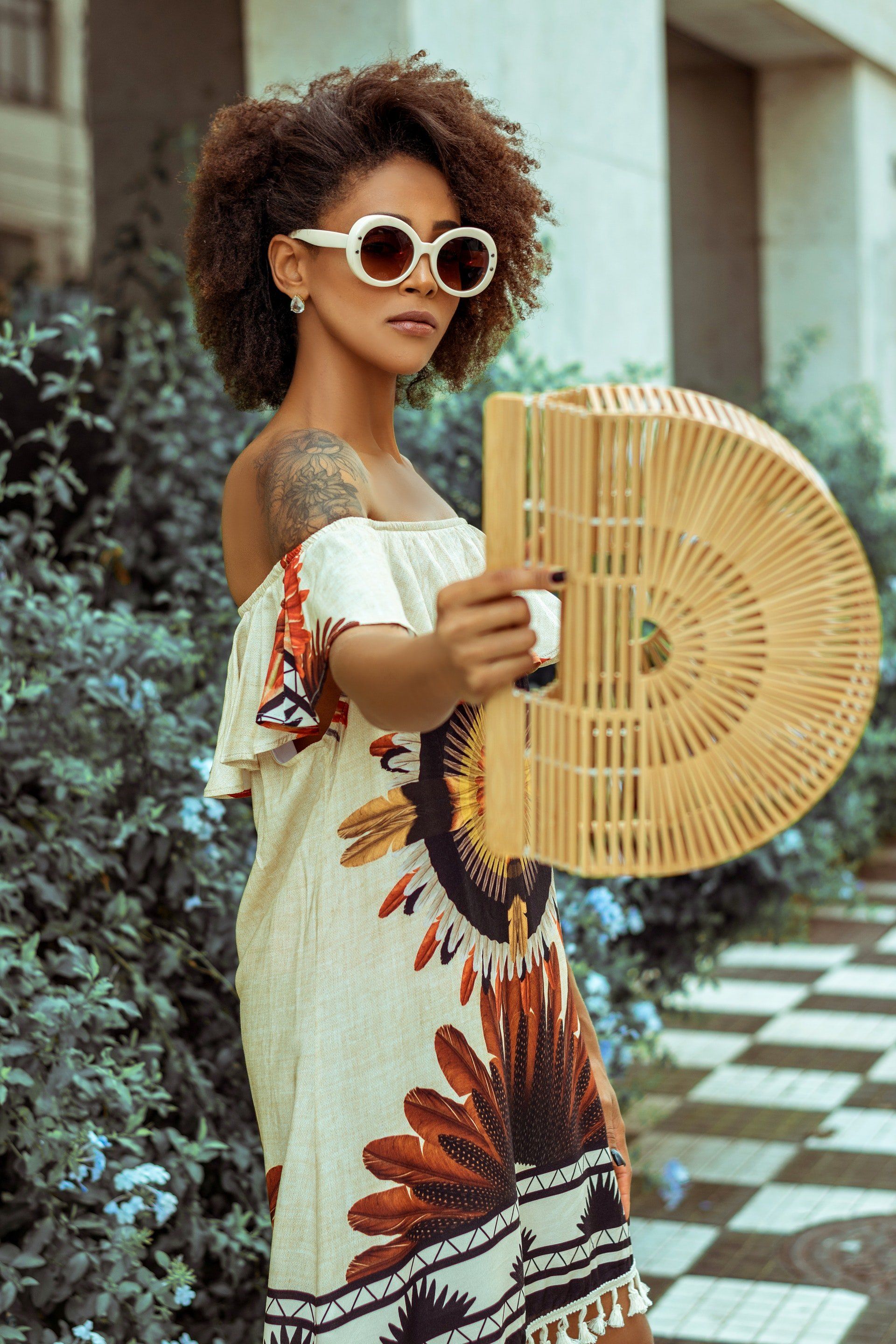 Une femme vêtue d’une robe et de lunettes de soleil tient un éventail en bois.