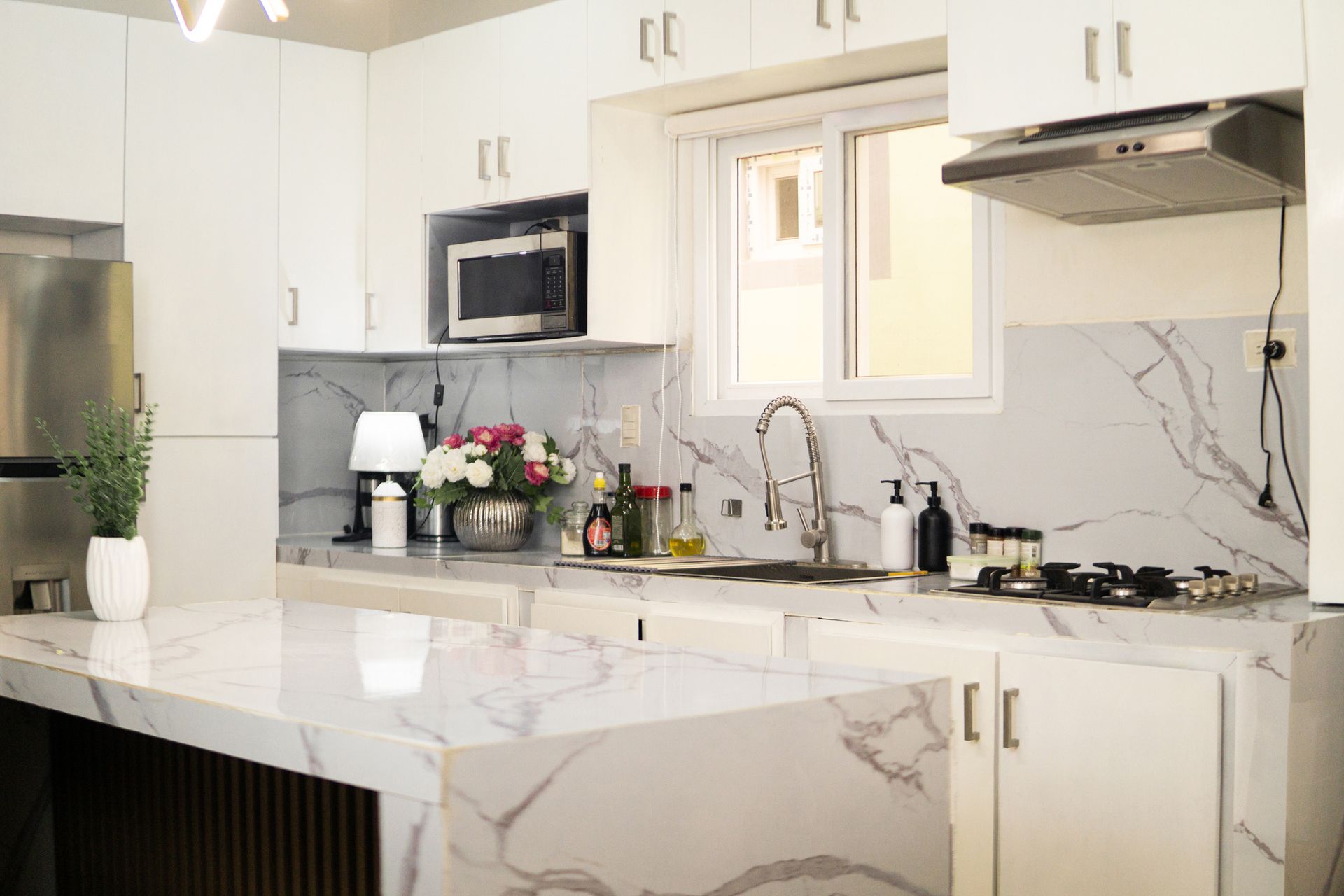 A luxury kitchen with a quartz waterfall island, stainless steel appliances, and white cabinets.