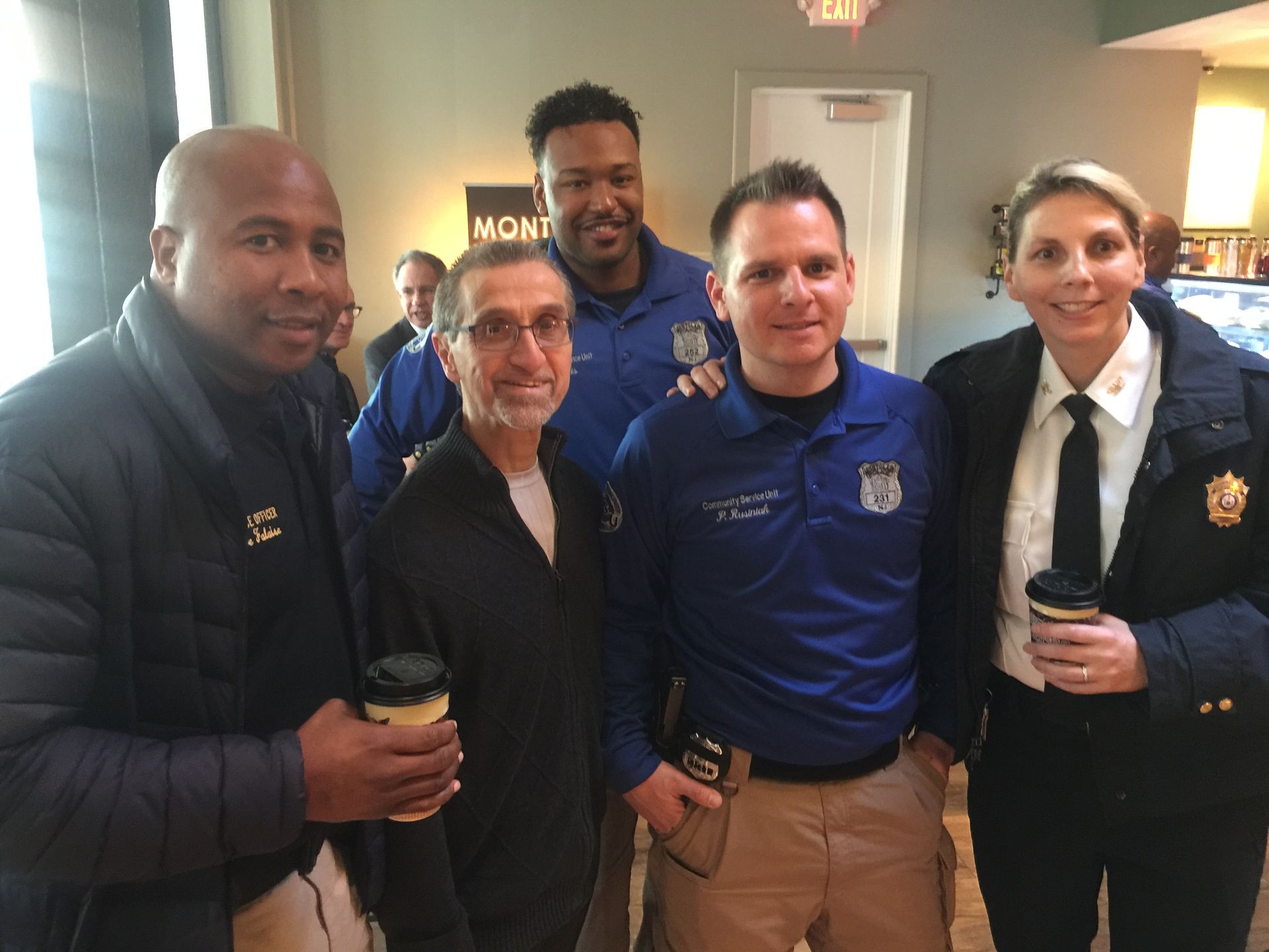 Group of people in blue uniforms pose, holding coffee cups indoors.