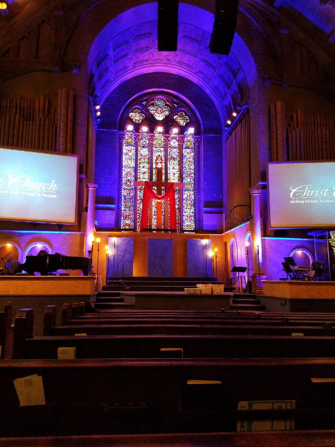 Interior of church with stained glass, stage, and purple lighting. Rows of pews.