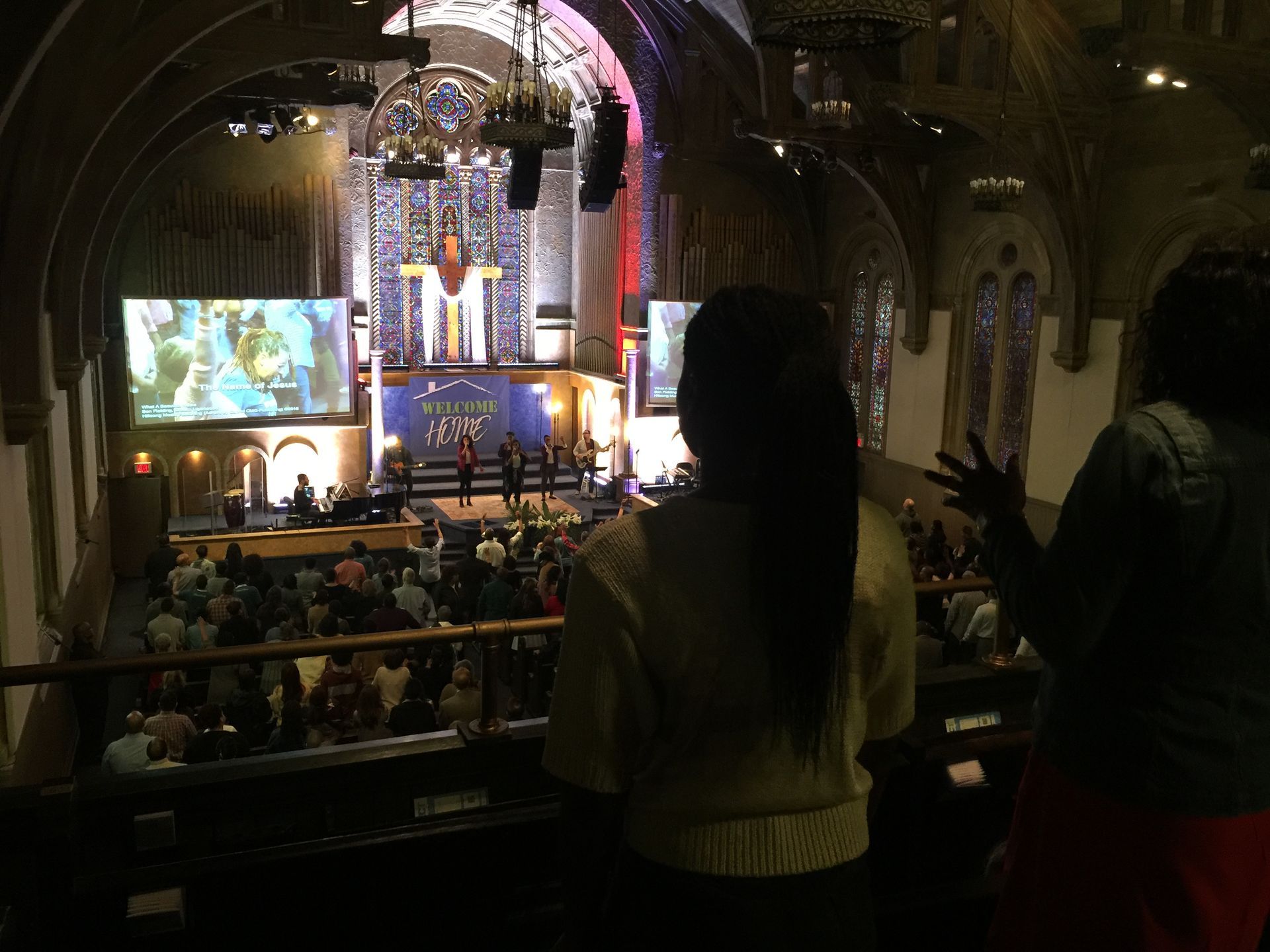 People in a church auditorium, stage lit with screens. Two women stand in the foreground.