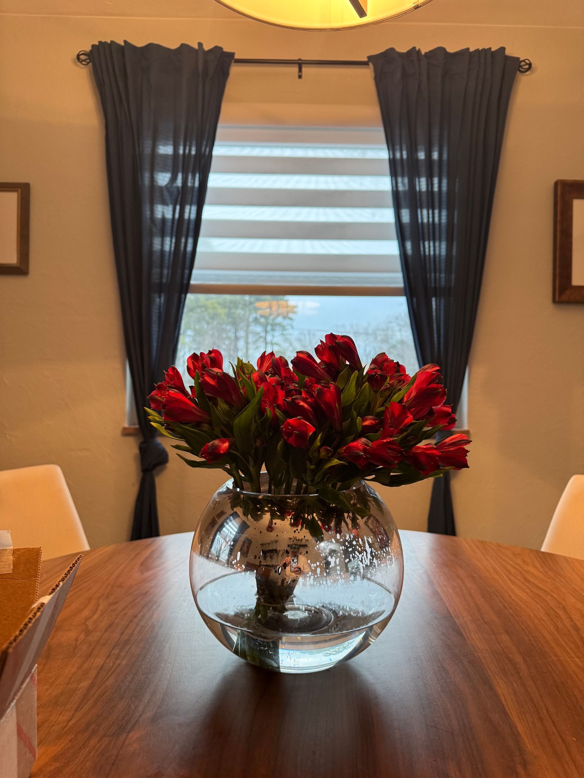 A vase filled with red flowers sits on a wooden table in front of a window.