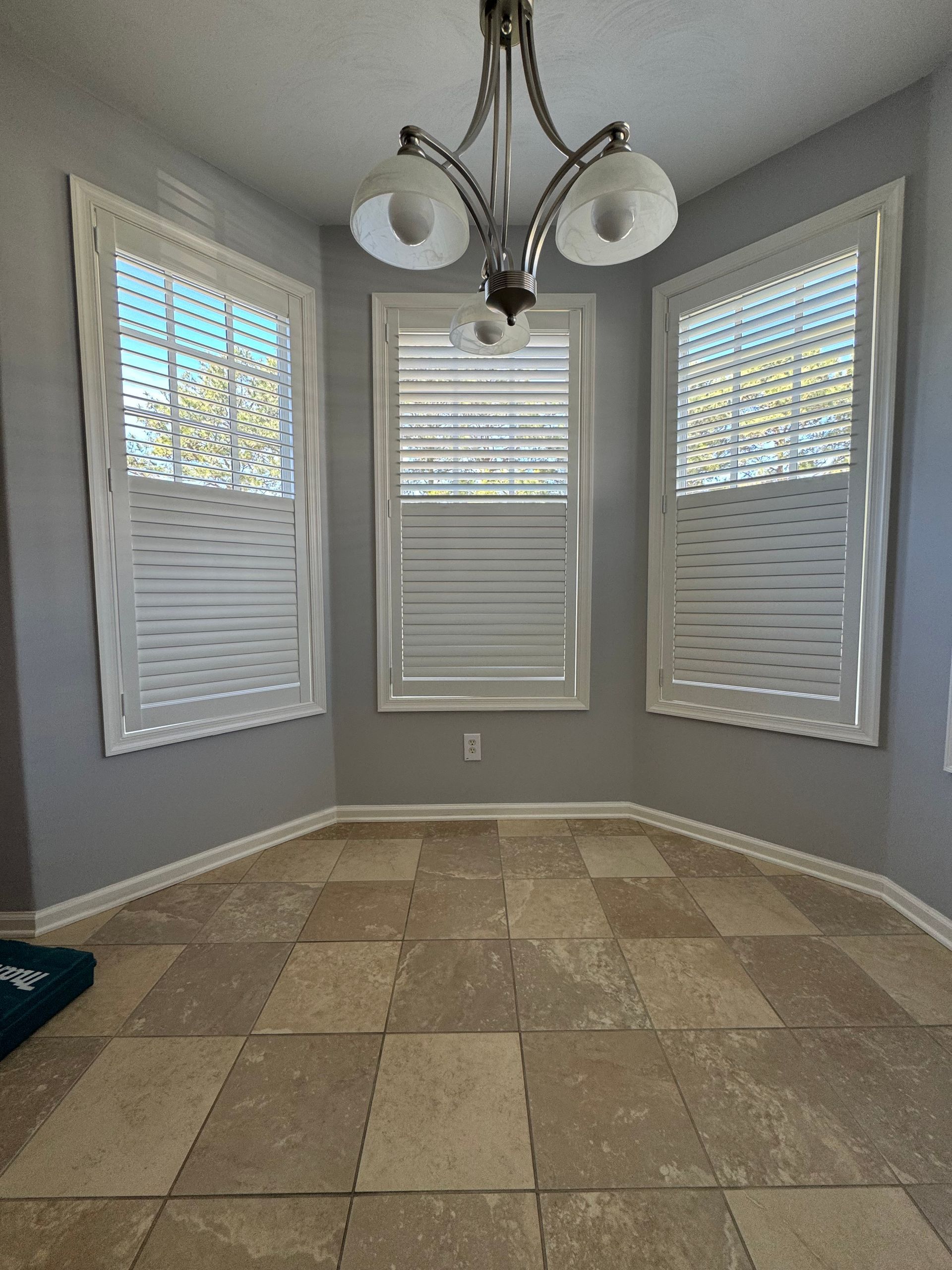 An empty room with a chandelier and shutters on the windows.