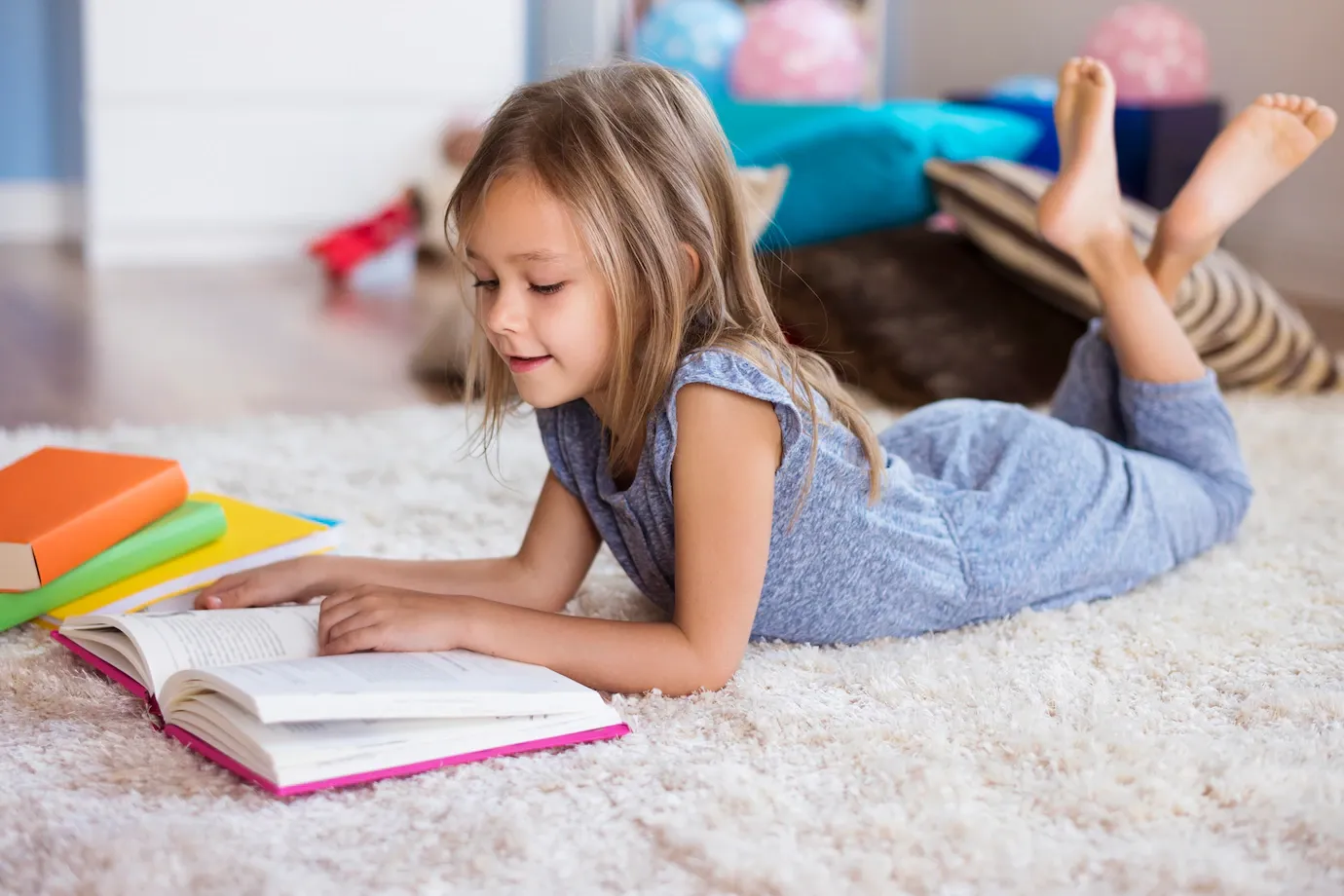 A little girl is laying on the floor reading a book.