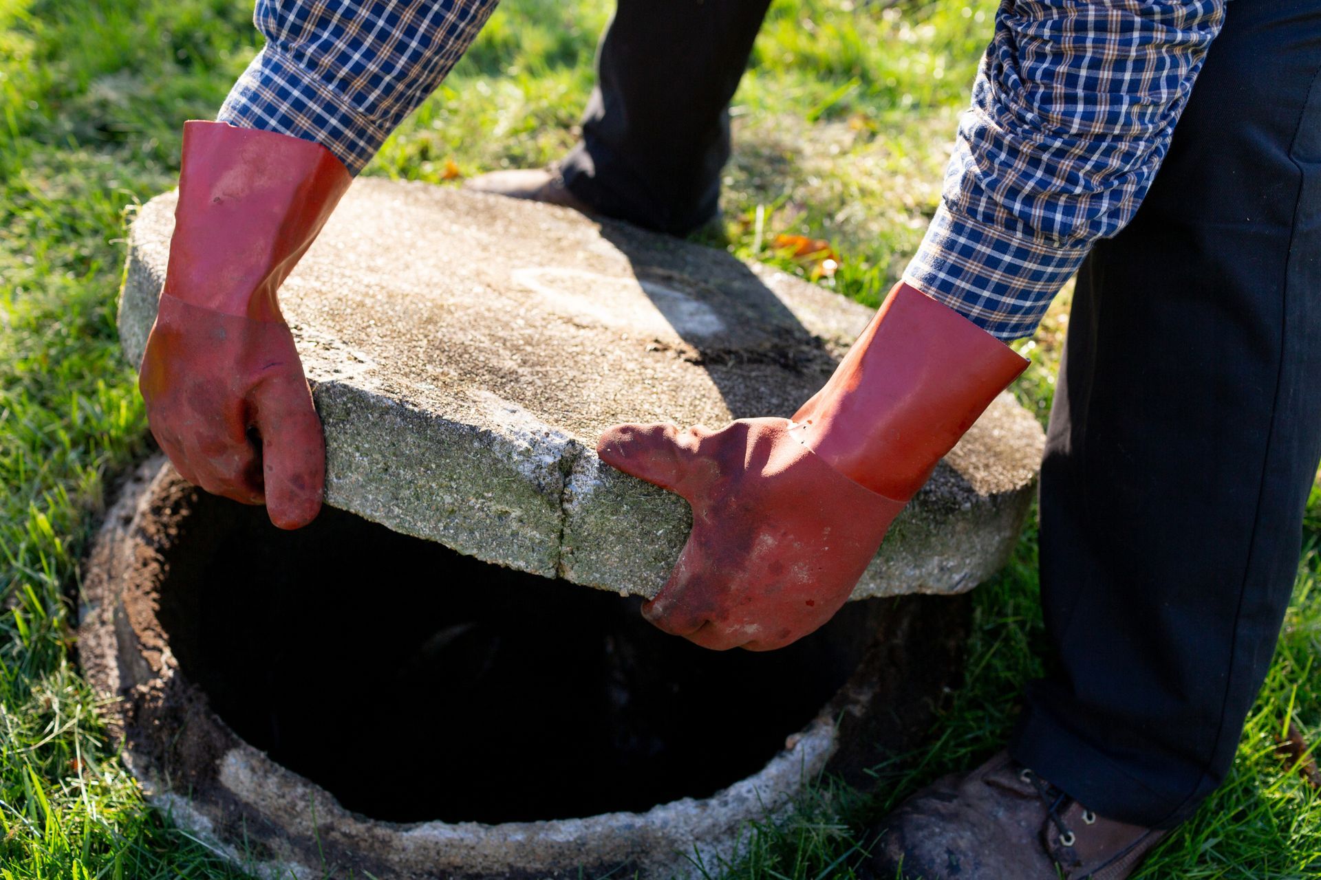 Plumber in gloves lifting up cover of septic tank