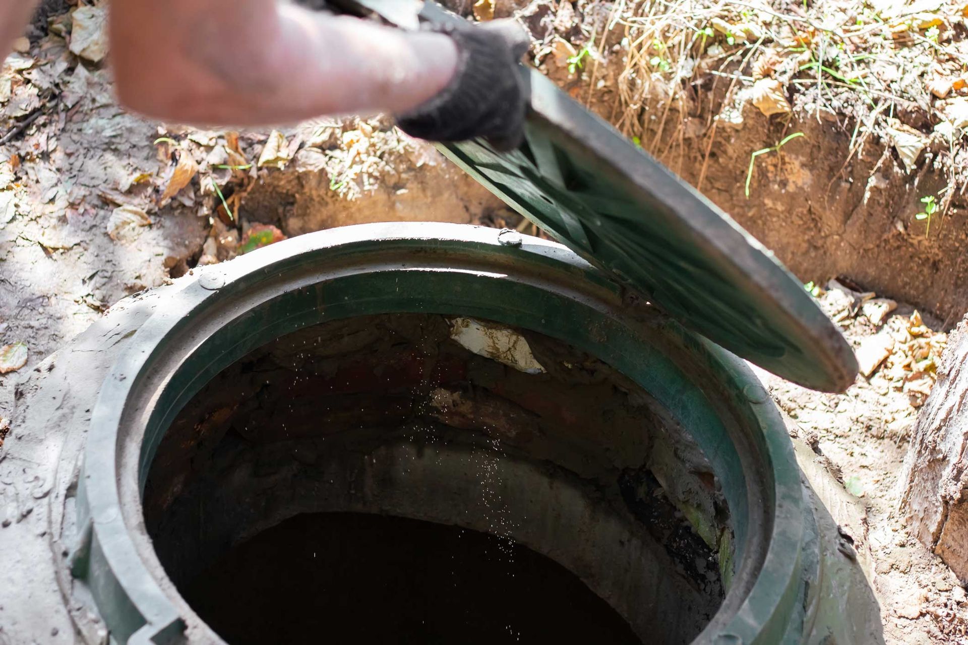 Gloved hands open a septic system tank on the ground to perform professional repair and maintenanc