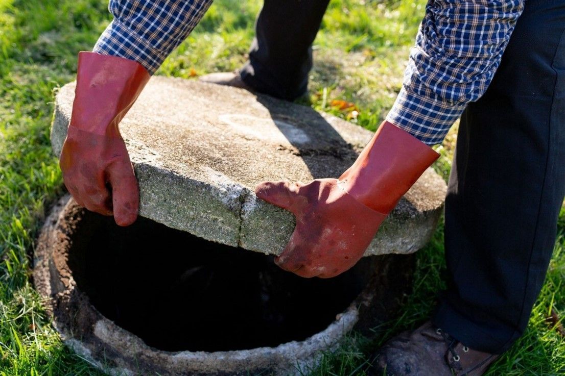 A person wearing red gloves lifting a concrete cover off a septic tank