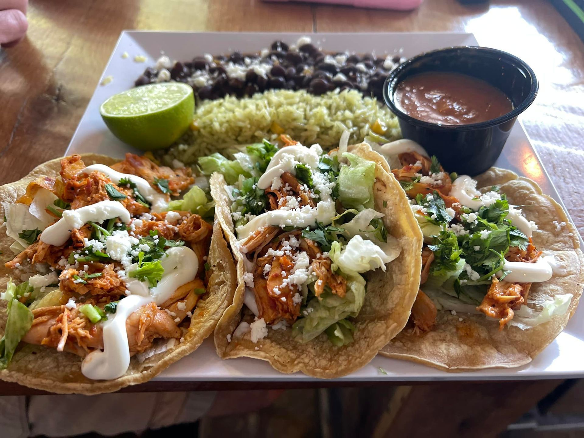 A plate of tacos , guacamole , black beans and rice on a table.