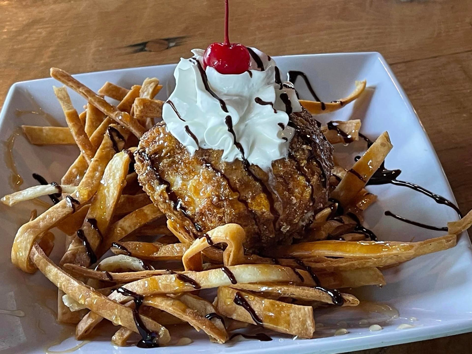 A white plate topped with french fries and a dessert with whipped cream and a cherry on top.