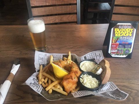 A plate of fish and chips with a glass of beer on a table.