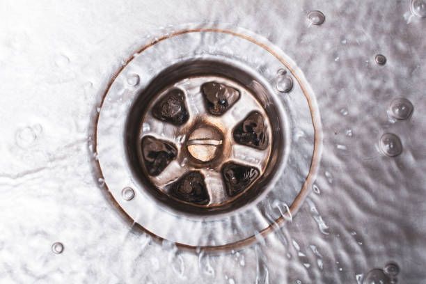 Water draining down a kitchen sink, viewed from above, with a metal drain and bubbling water.