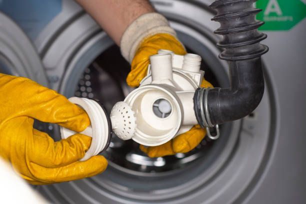 Hands in yellow gloves removing a part from a washing machine.