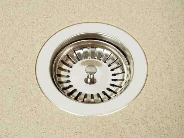 Stainless steel sink drain with a strainer, set in a beige countertop.