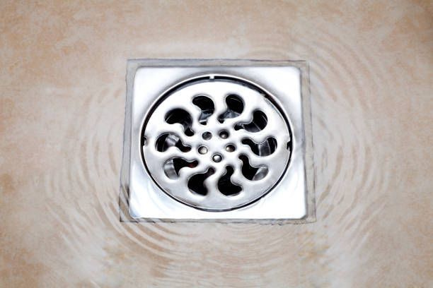 Shower drain with swirling water, surrounded by tan-colored tile.