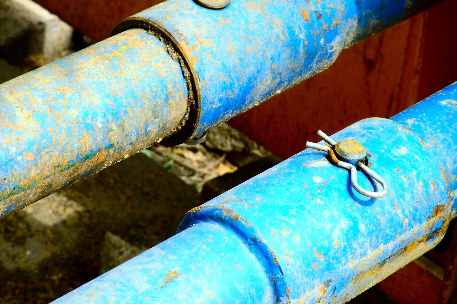 Two rusty blue pipes connected, secured by metal pins, against an orange background.