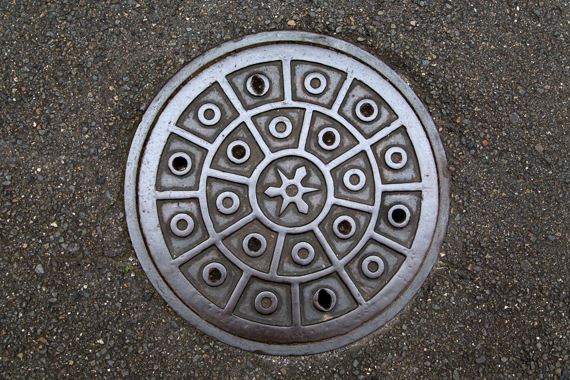 Circular, patterned manhole cover on asphalt.