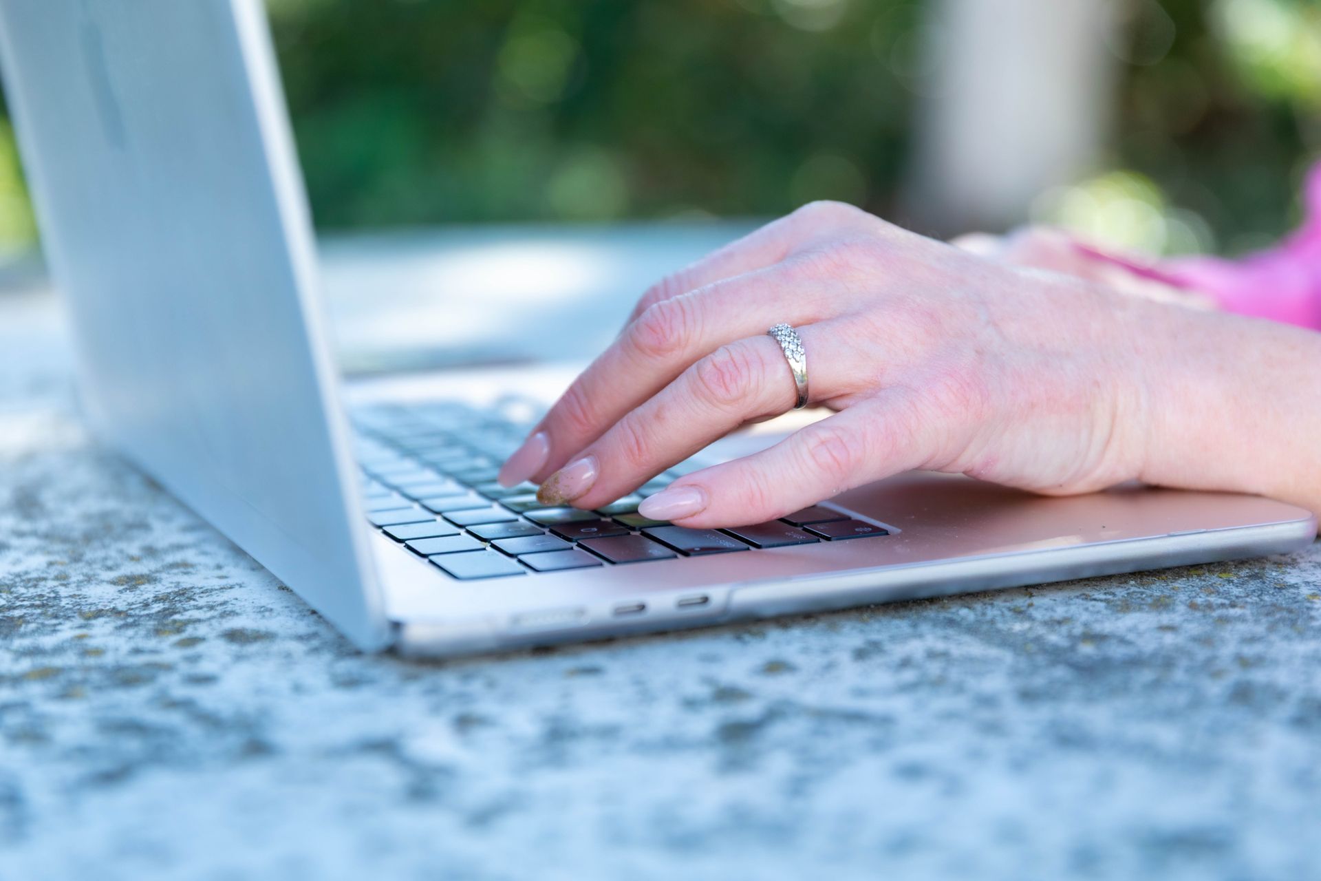 Hand typing on a laptop outdoors on a speckled table