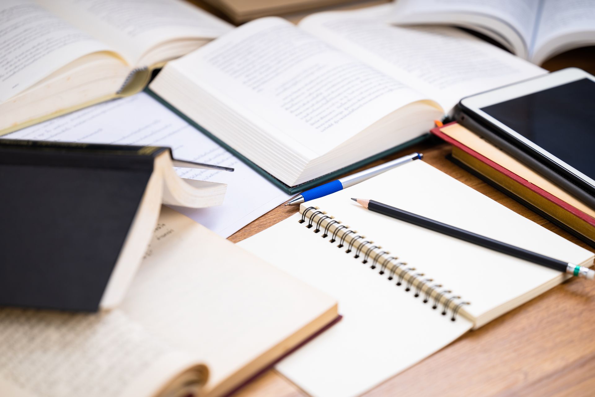 Open books and notebooks with pens and pencils on a wooden desk.