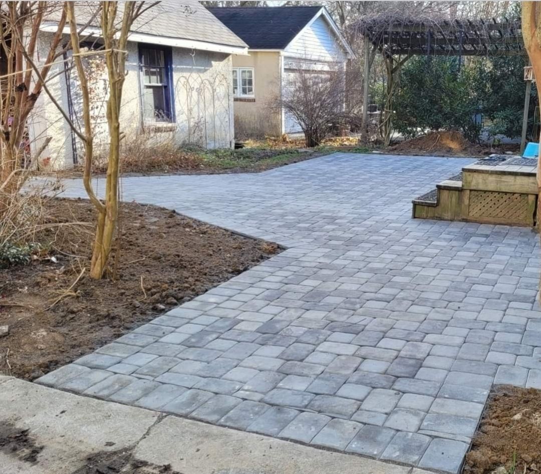 Brick patio with small building in the background. Paved path leads up to steps.