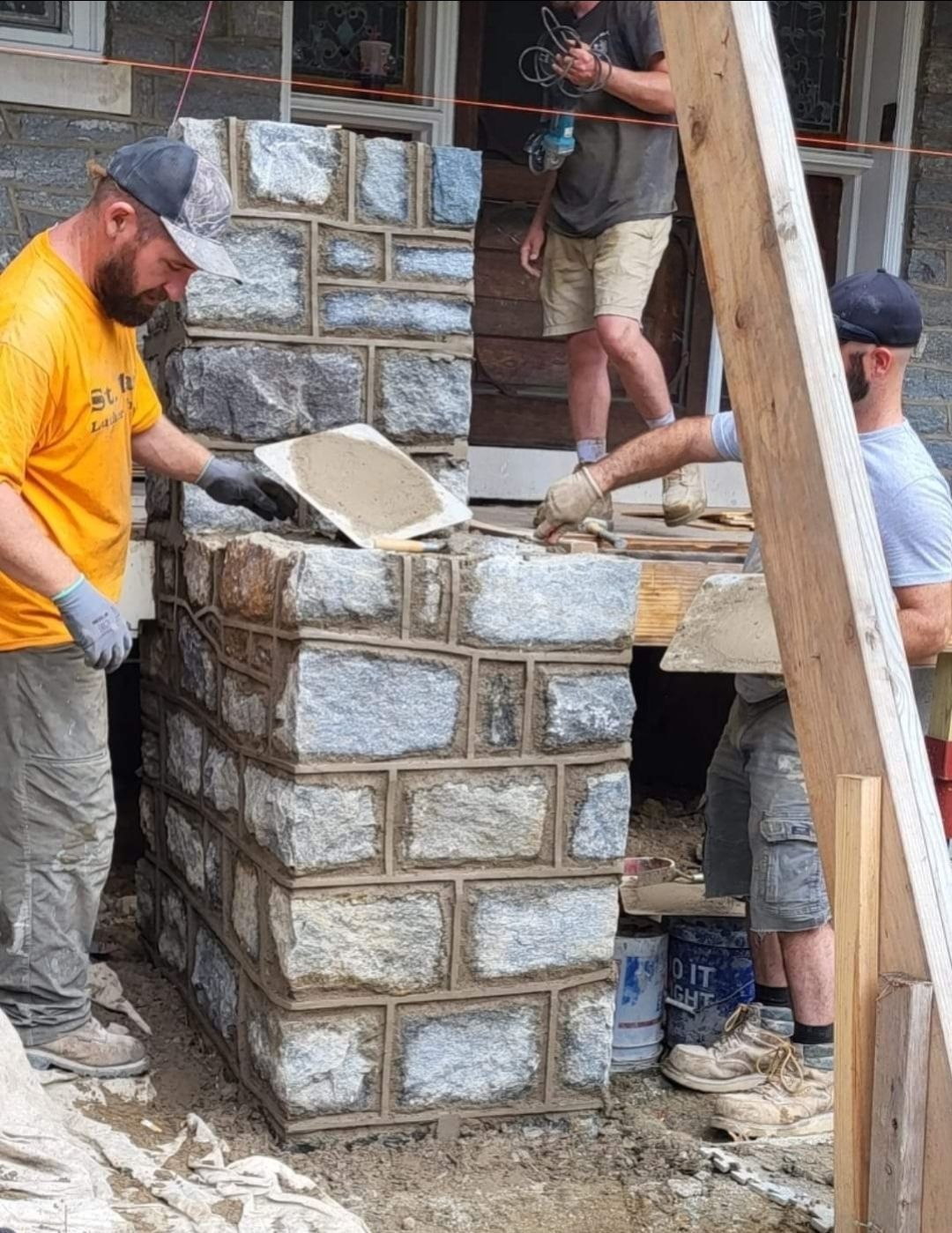 Stone masons constructing a stone wall outside a building, applying mortar between the stones.
