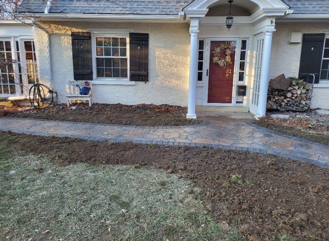 House front with a brick path, leaves, and a red door.