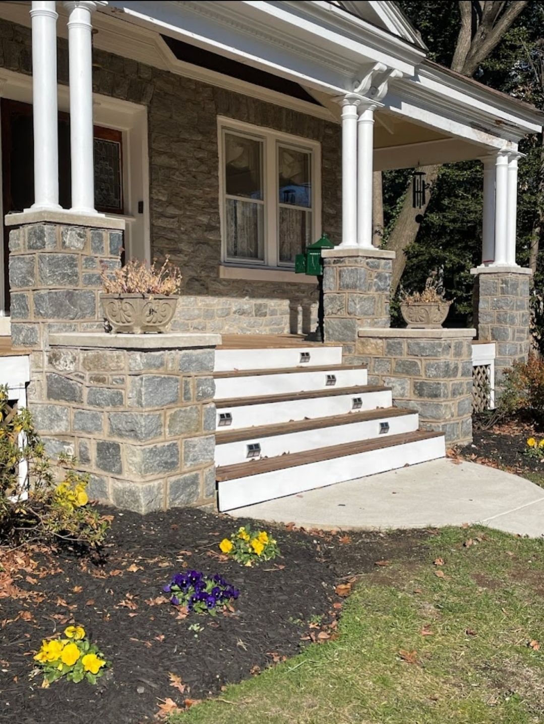 Stone steps leading to a house with a covered porch, surrounded by landscaping.