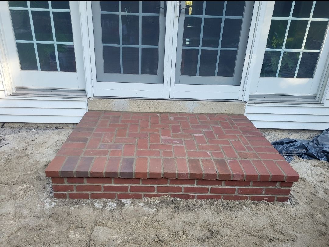 Brick step in front of white-framed doors. Tan ground surrounds the step.
