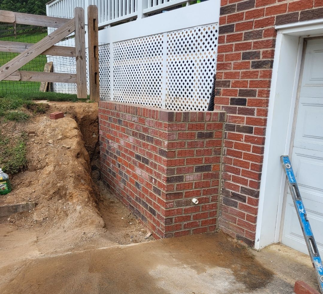 Brick wall foundation next to a garage door and white lattice on a sloped yard.