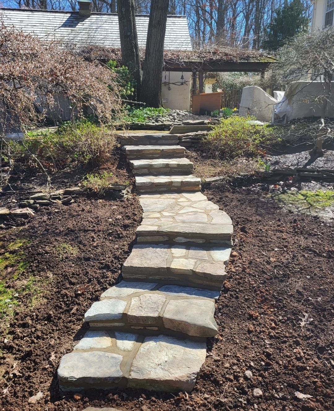Stone steps leading uphill through a landscaped garden; brown mulch, green plants.