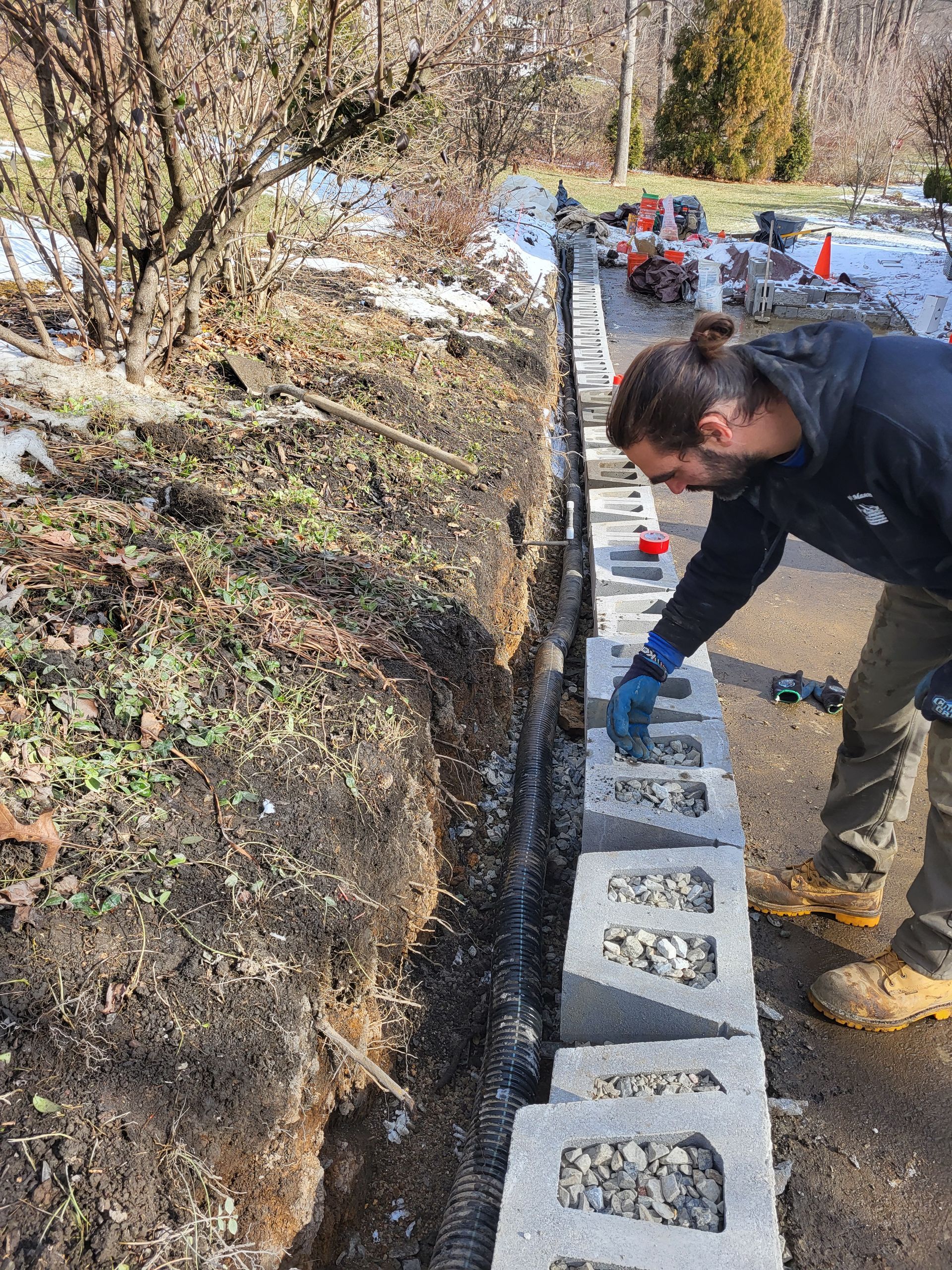 Man building a retaining wall with cinder blocks in an outdoor setting.