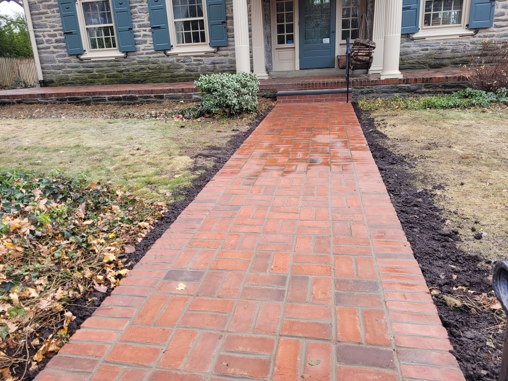 Brick walkway leading to a house with blue shutters and a white porch.