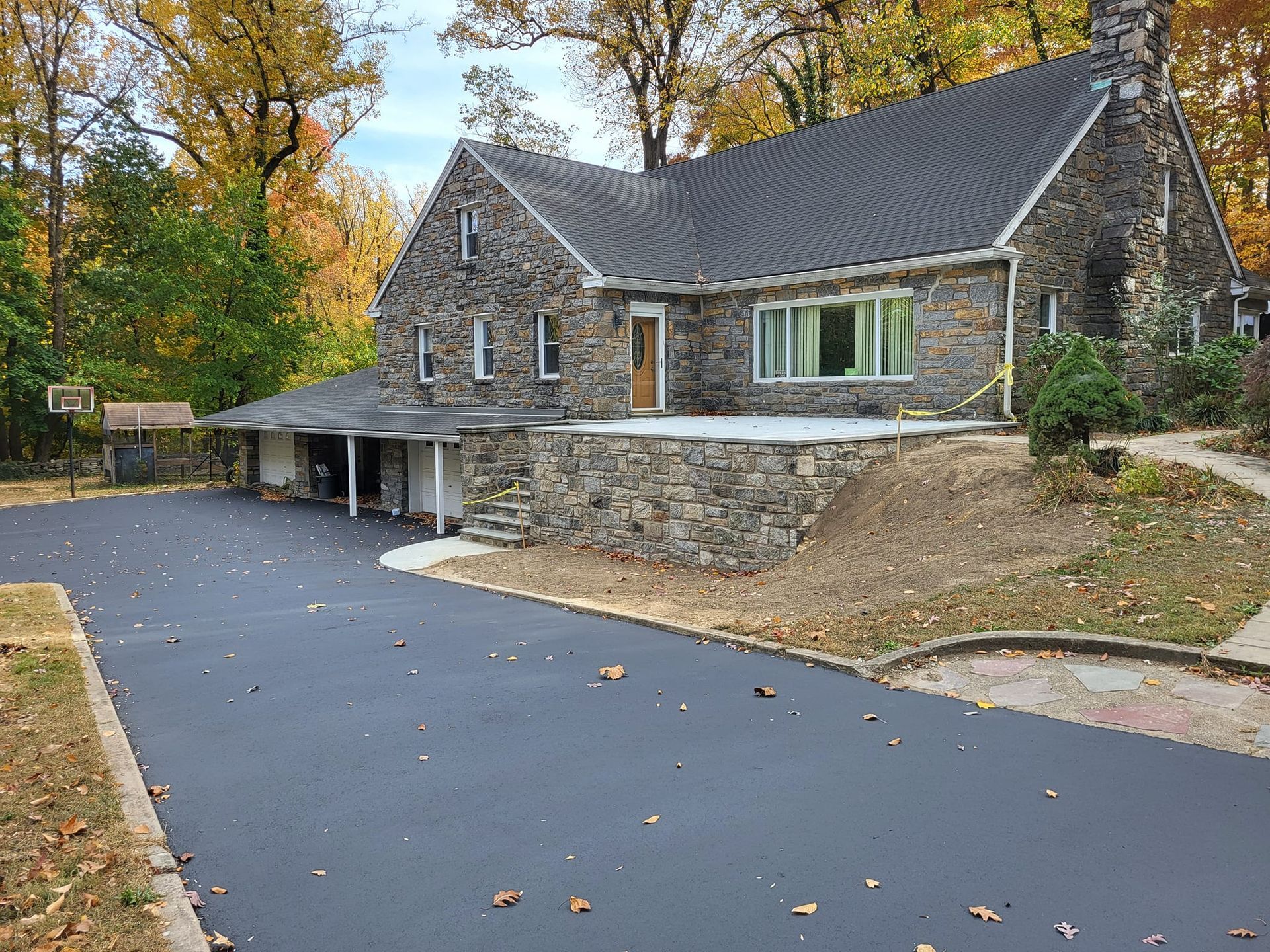 Stone house with black asphalt driveway and autumn foliage.