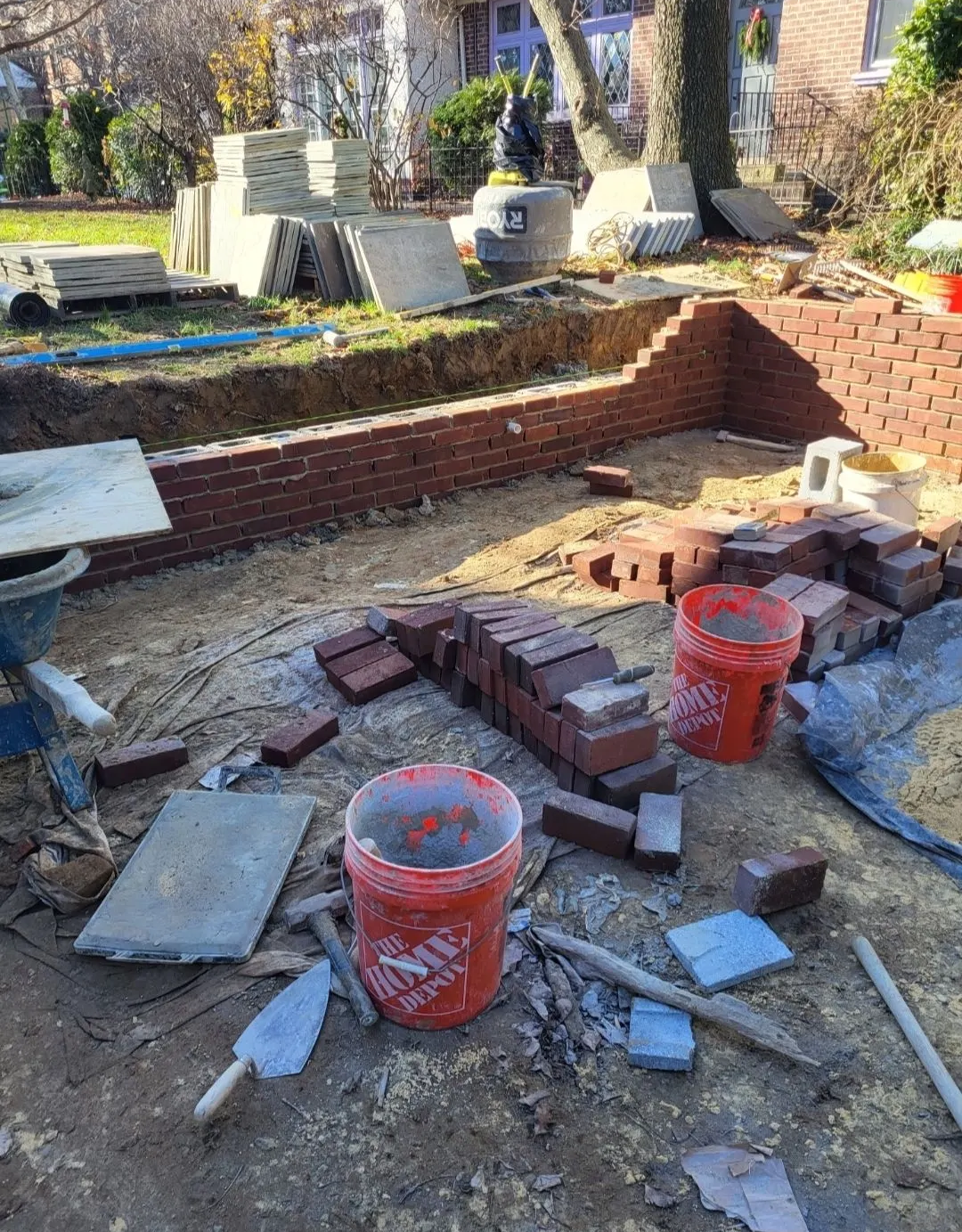 Bricklaying project outdoors with bricks, mortar buckets, tools, and a partially built wall.