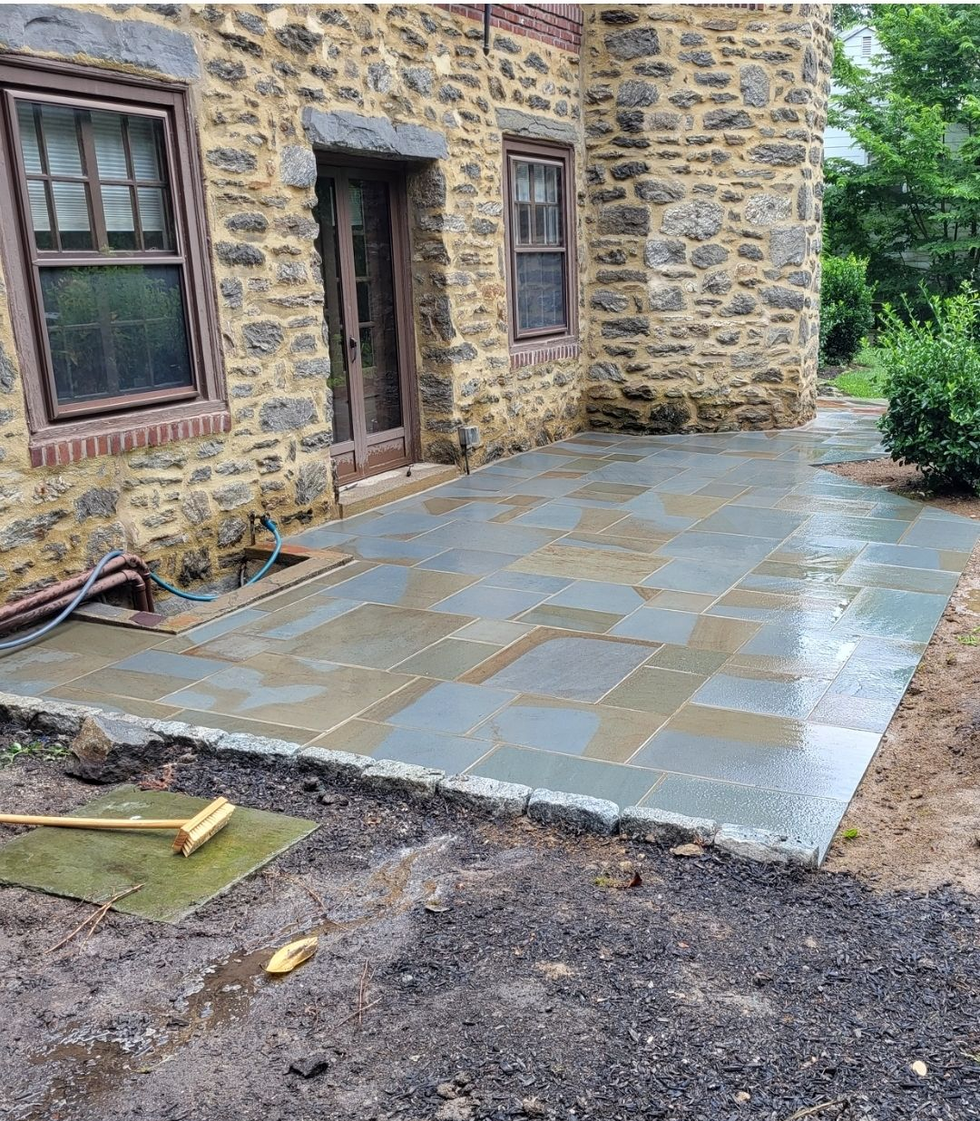 Stone patio outside a stone building with windows and a door; wet flagstone pavers.