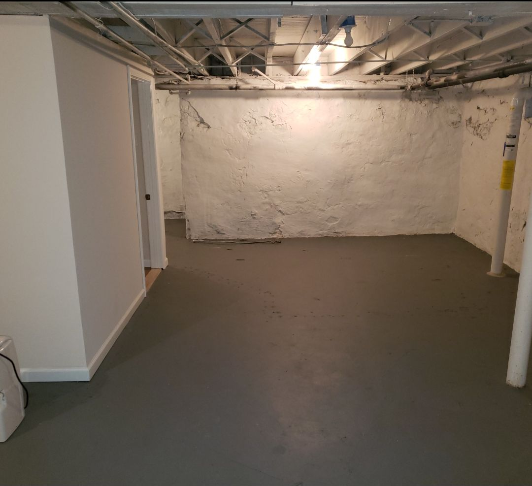 Basement room with concrete floor, white walls, and exposed ceiling beams.
