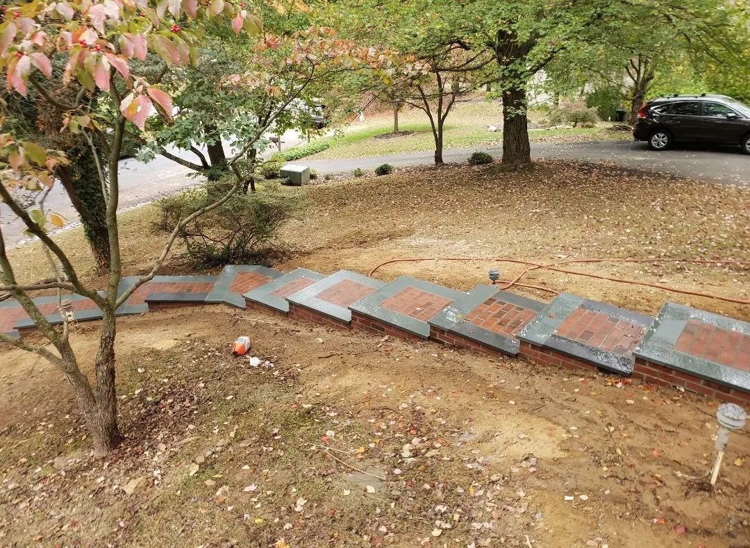 Brick steps descending a grassy slope towards a road. Trees and a parked car are in the background.