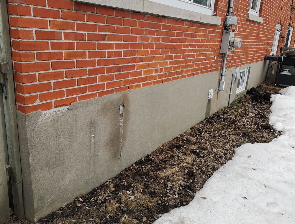 Brick building with a concrete foundation, a small window, and snow.