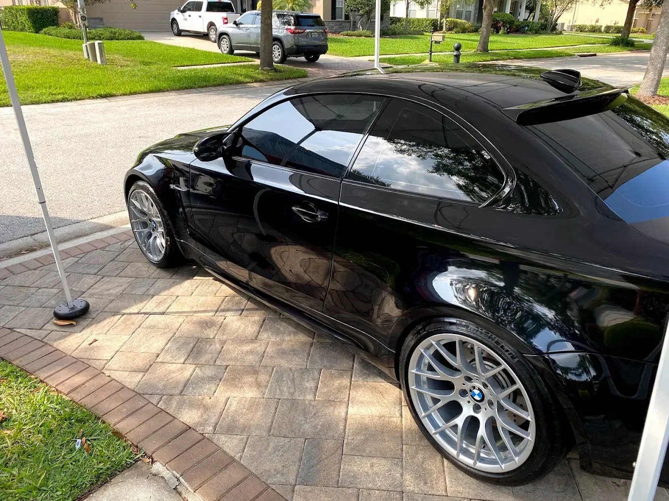 Black BMW coupe parked on a paved driveway, with silver rims and tinted windows.