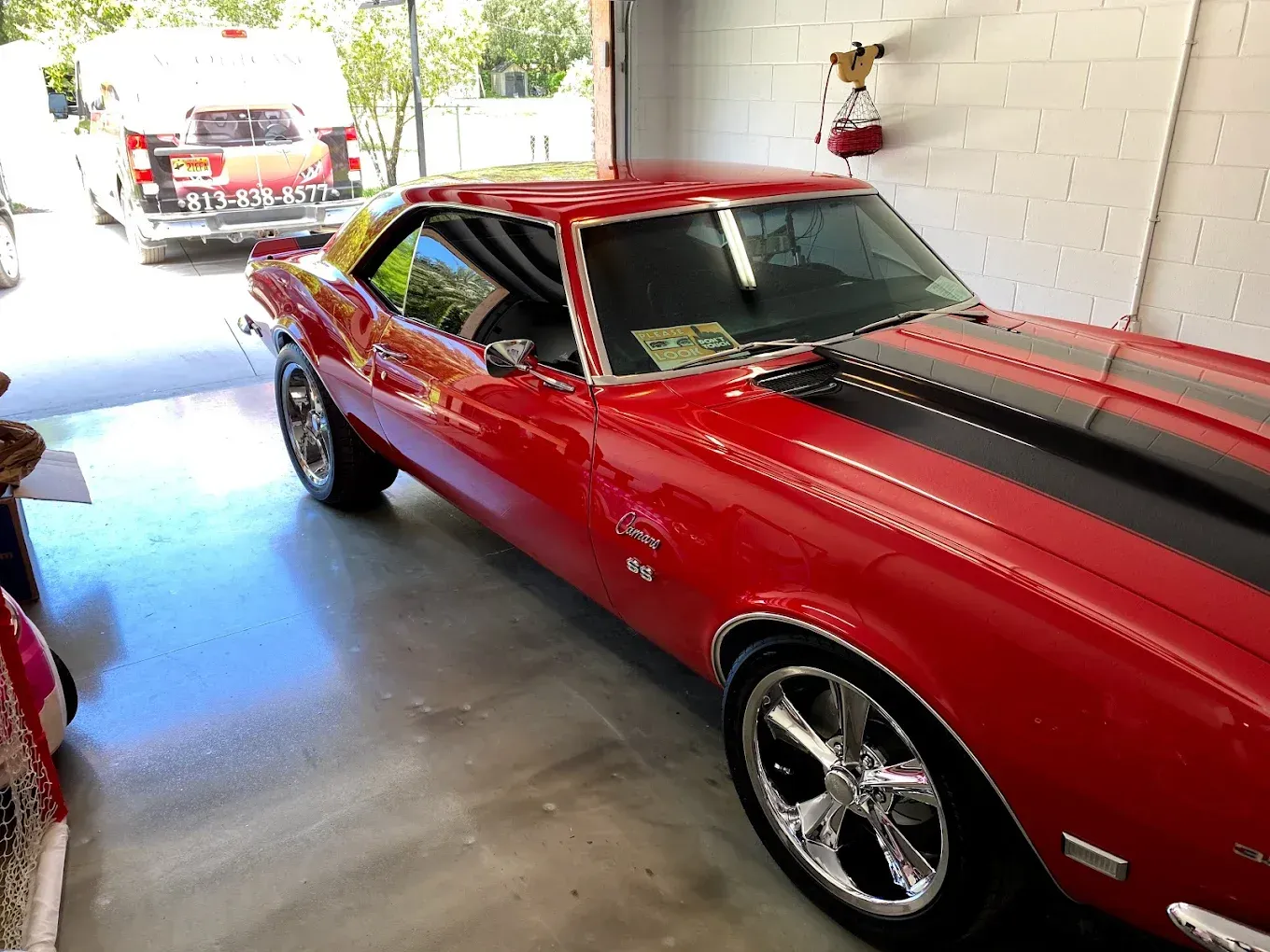 Red classic Camaro with black racing stripes in a garage.