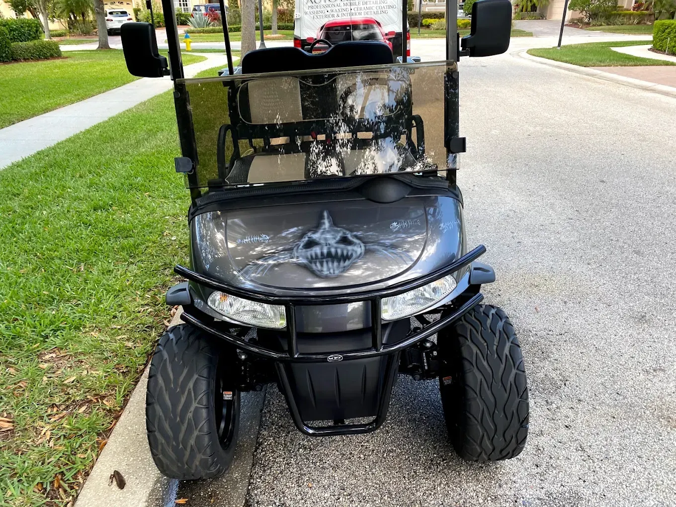 Black custom golf cart with a shark graphic on its hood, parked on a curb near a street.
