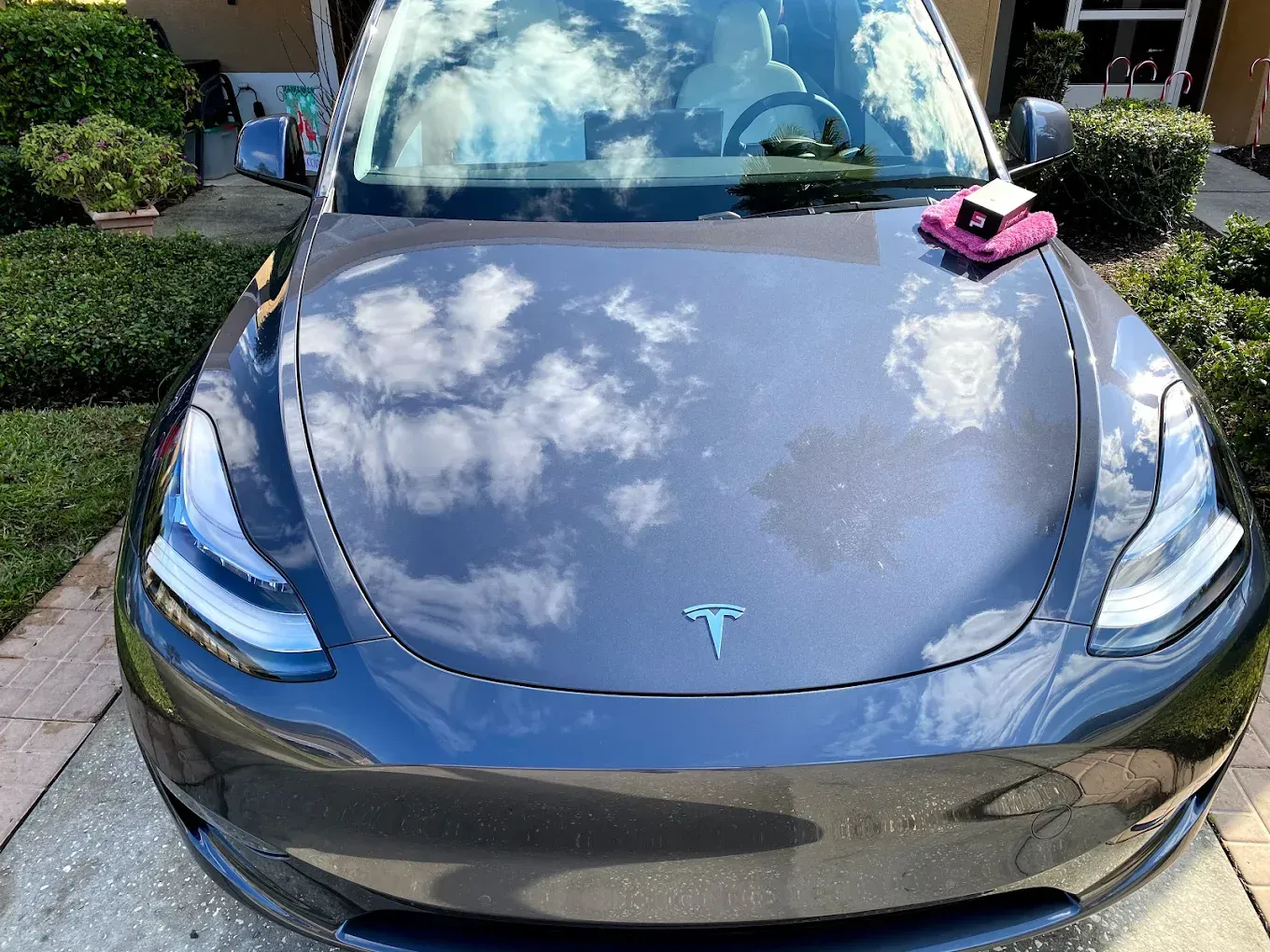 A shiny, gray Tesla car hood reflecting clouds with a pink cloth and a small gadget on top.